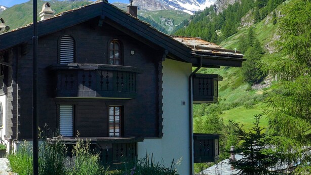 A traditional chalet with a balcony, set against a backdrop of a mountain and lush greenery. - Lovely apartment for 4 people with WIFI and TV (Zermatt)