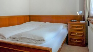 A neatly made bed with white linens in a room with a wooden headboard and a wooden nightstand with drawers and a lamp. - Lovely apartment for 4 people with WIFI and TV (Zermatt)