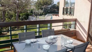 A balcony with a table set for dining, overlooking a garden and a building. - Beautiful apartment for 4 people with pool, WIFI, A/C, TV and terrace (Fréjus)