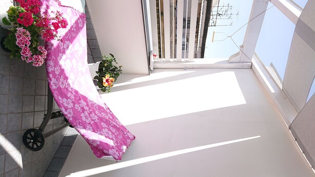A balcony with a pink floral tablecloth, potted plants, and a view of the sky and buildings. - Wide Apartment with Terrace in City Center (Napoli)