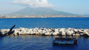 A coastal view with a rocky breakwater, a boat, and a distant mountain. - Wide Apartment with Terrace in City Center (Napoli)