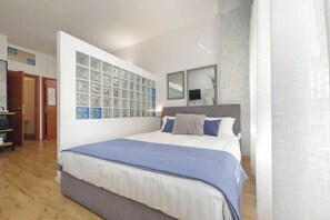 Ein Schlafzimmer mit einem großen Bett, einem an der Wand befestigten Fernseher und einer Tür zu einem anderen Raum.