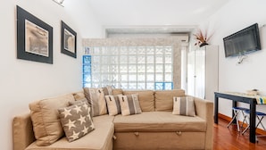 Un salon avec un canapé d’angle beige, un téléviseur fixé au mur et une fenêtre agrémentée d’un paravent décoratif.