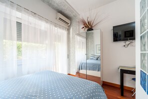 Une chambre à coucher avec un lit, un miroir, une télévision et une fenêtre ornée de rideaux légers.