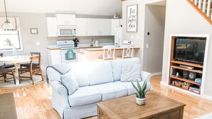 Un salon moderne avec un canapé à rayures, une table basse en bois et un meuble TV agrémenté de livres et d’objets décoratifs.