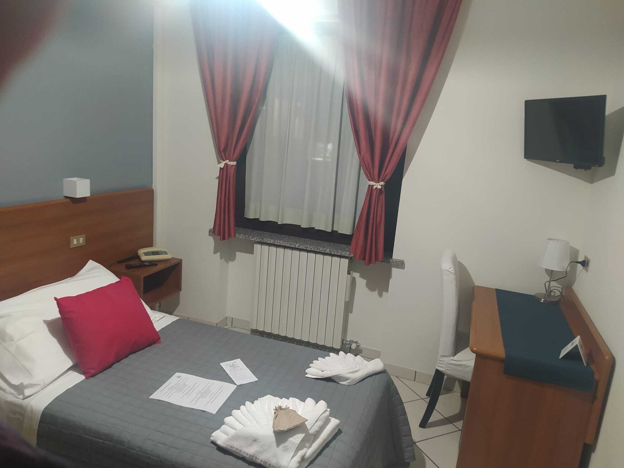 Ein Hotelzimmer mit Bett, Nachttisch, Schreibtisch, Stuhl, Fernseher und einem Fenster mit Vorhängen.