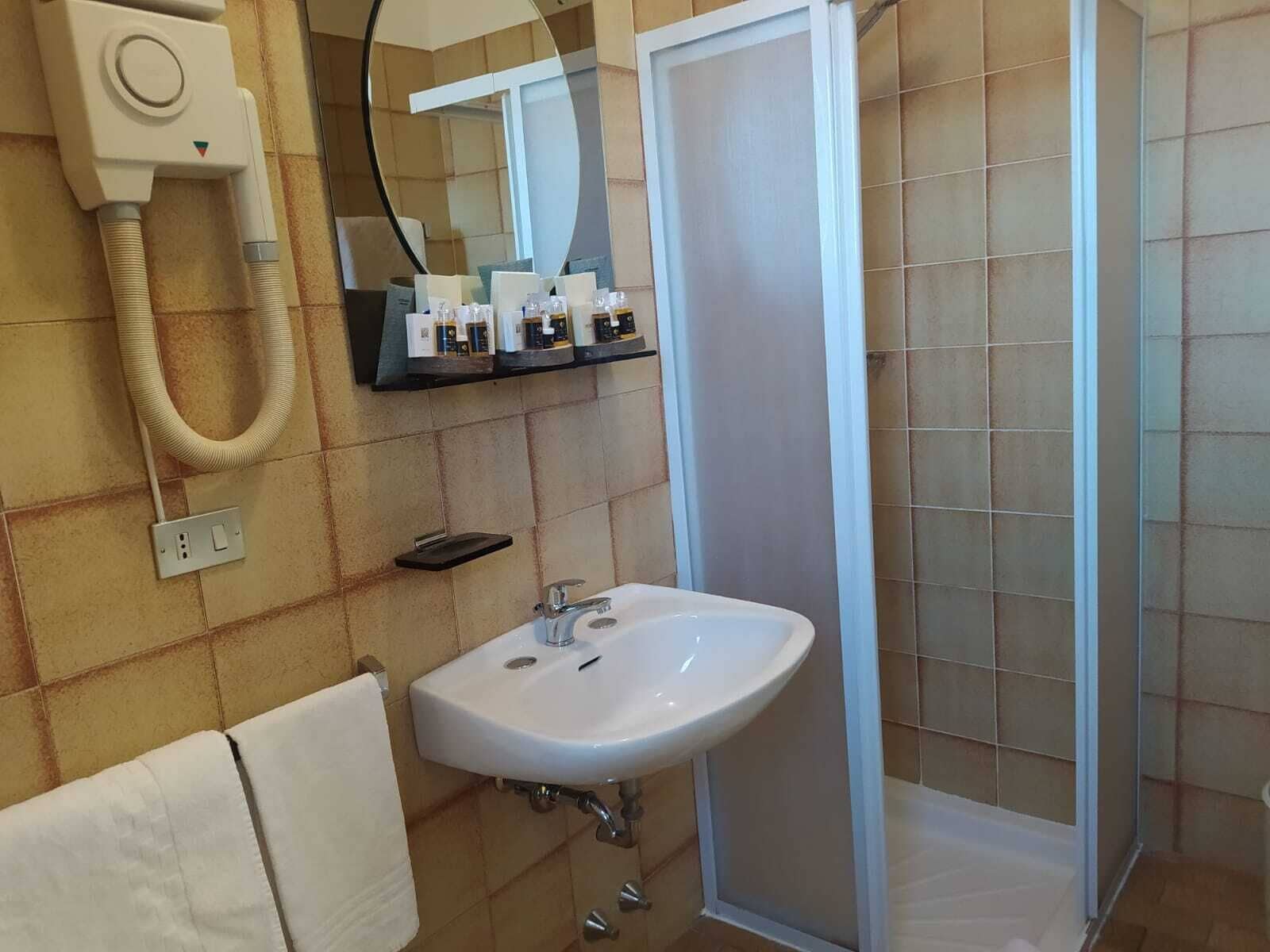 Ett badrum med ett vitt handfat, en spegel, en hårtork och en dusch.