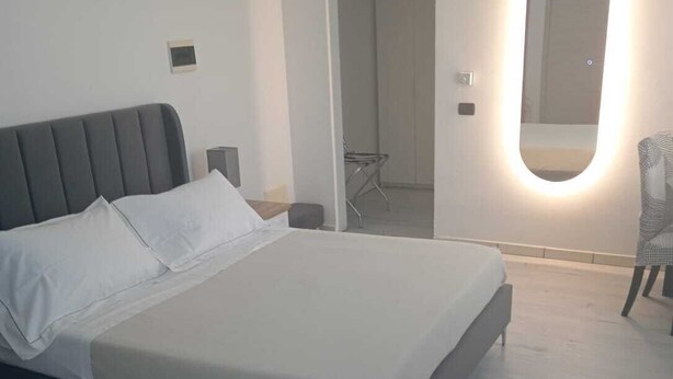 Une chambre à coucher moderne avec un grand lit, une table de chevet, une chaise et un miroir avec un éclairage intégré.