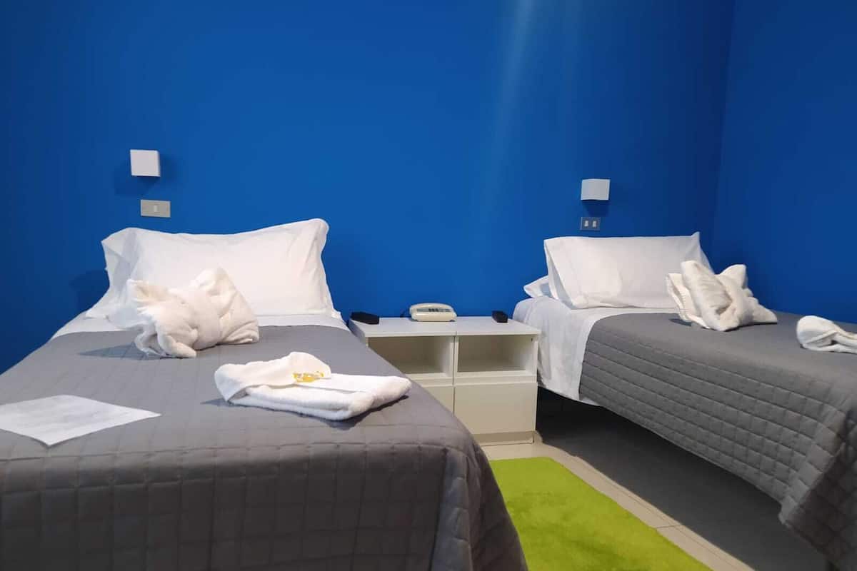 A hotel room with two beds, each with white linens and pillows, a small bedside table with a phone, and a green rug.
