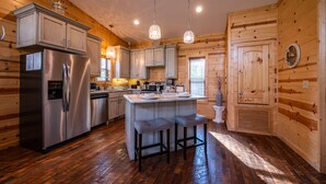A modern kitchen with wooden walls, stainless steel appliances, and pendant lighting. - Luxury Honeymoon cabin, jetted tub, tile shower, hot tub, fire pit (Broken Bow)