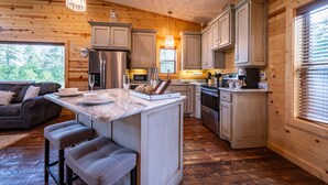 A wooden cabin interior with a kitchen island, bar stools, and a dining table. - Luxury Honeymoon cabin, jetted tub, tile shower, hot tub, fire pit (Broken Bow)