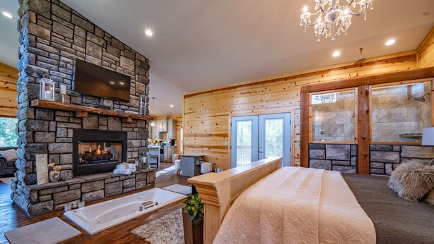 A spacious bedroom with a stone fireplace, a large bed, and a bathtub. - Luxury Honeymoon cabin, jetted tub, tile shower, hot tub, fire pit (Broken Bow)