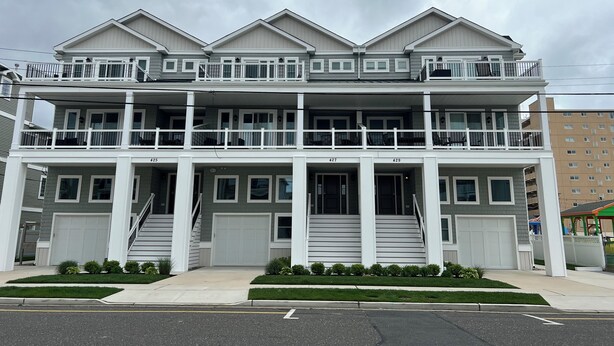 A multi-story residential building with a balcony on each floor, a central staircase, and a garage.