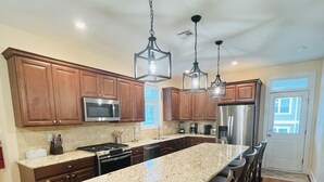 A kitchen with wooden cabinets, a stainless steel refrigerator, and a large island with bar stools.