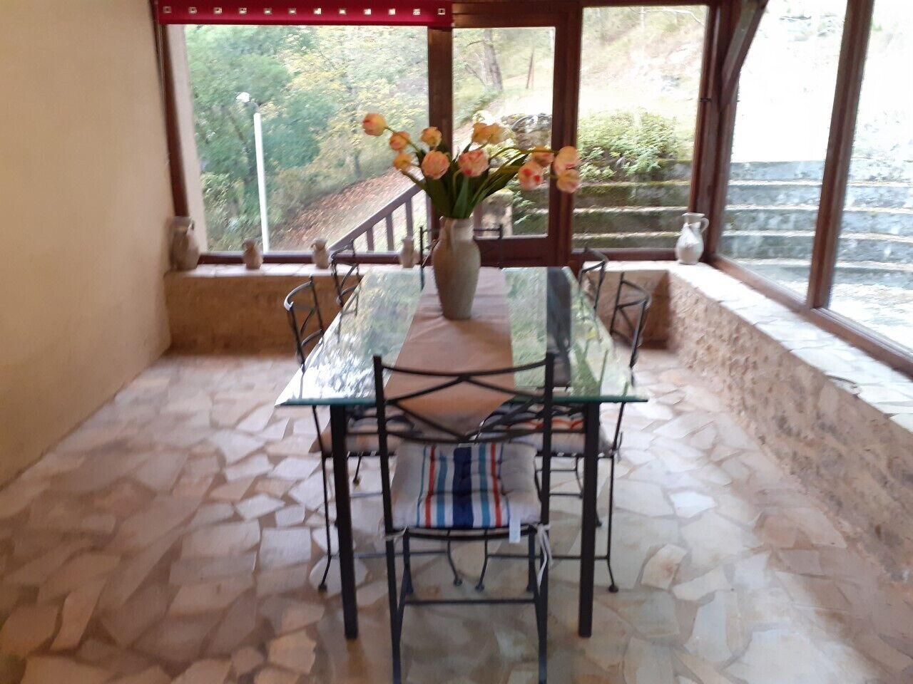 Een glazen tafel met stoelen, een vaas met bloemen en een stenen vloer.