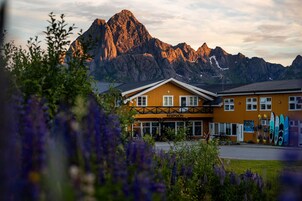 Un hotel con montañas al fondo, que presenta una fachada de madera y un cartel que dice 'RESEPSJON'.