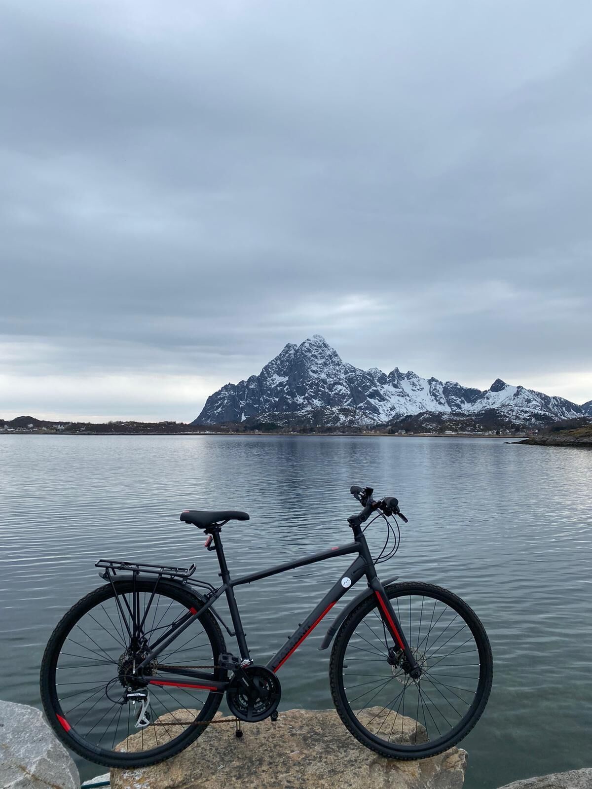 Un vélo tout-terrain est garé au bord d’un lac paisible, avec des montagnes enneigées en arrière-plan.