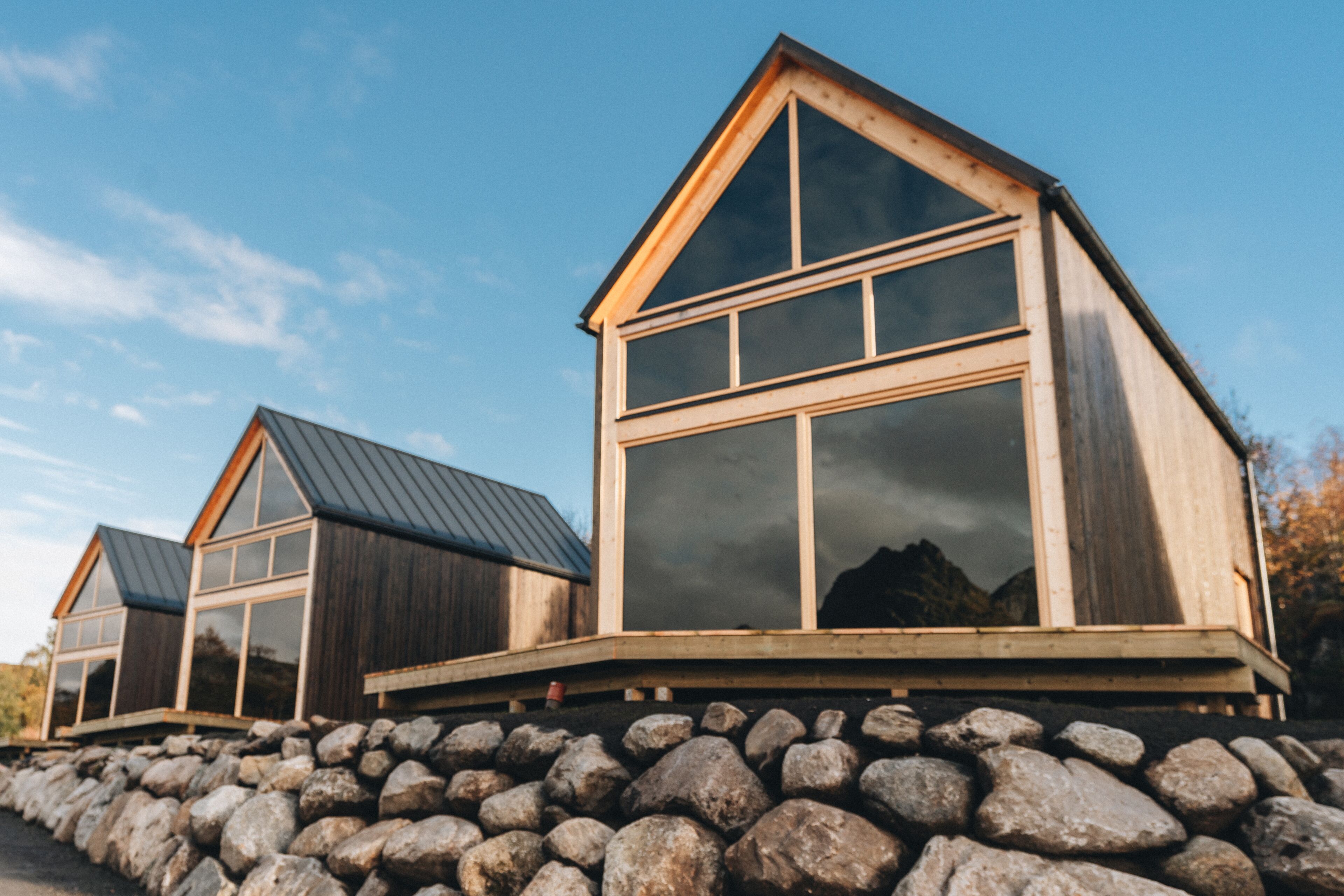 Una cabaña de madera con techo inclinado y ventanas amplias, asentada sobre una base rocosa.