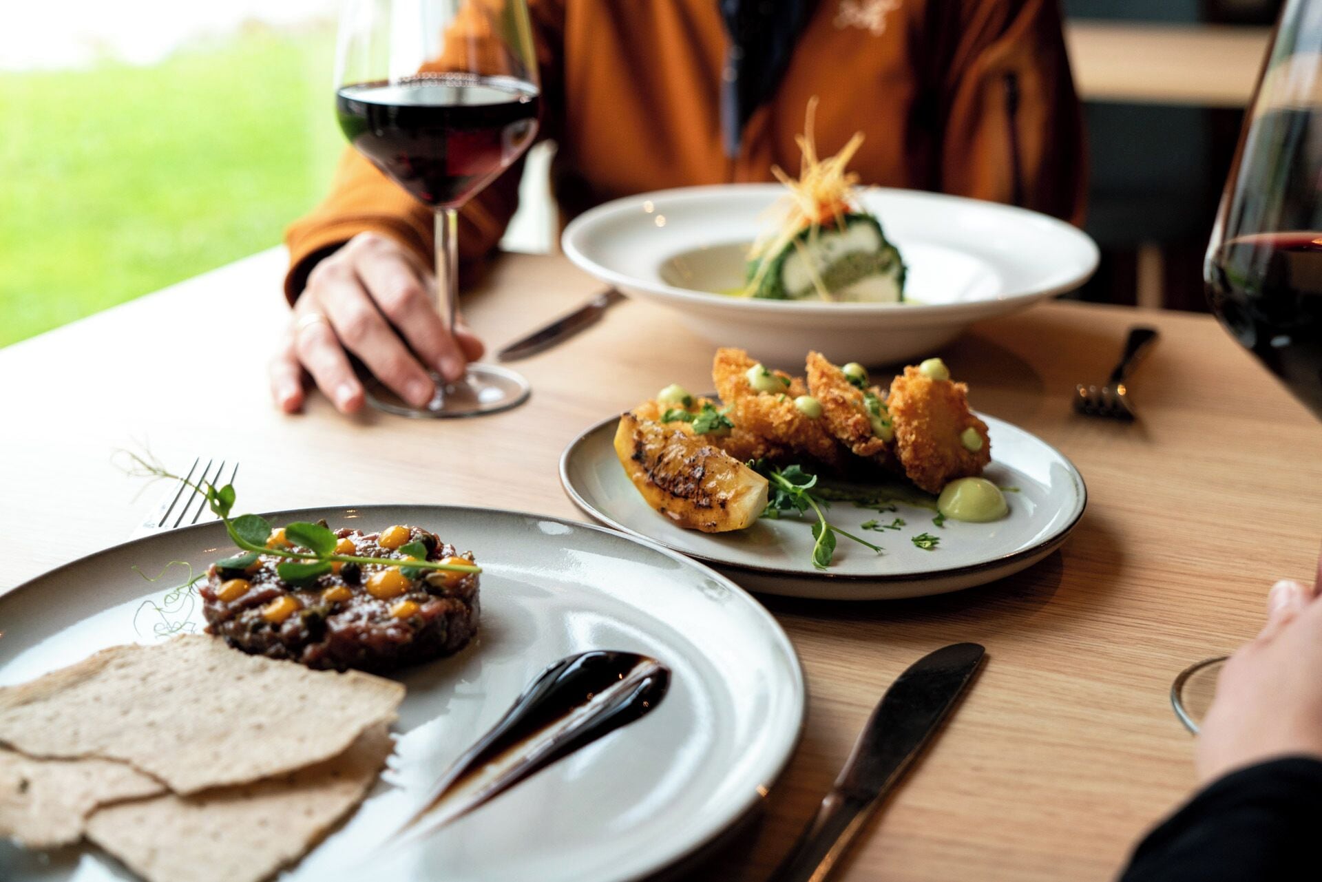 A dining table with plates of food, a wine glass, and cutlery.