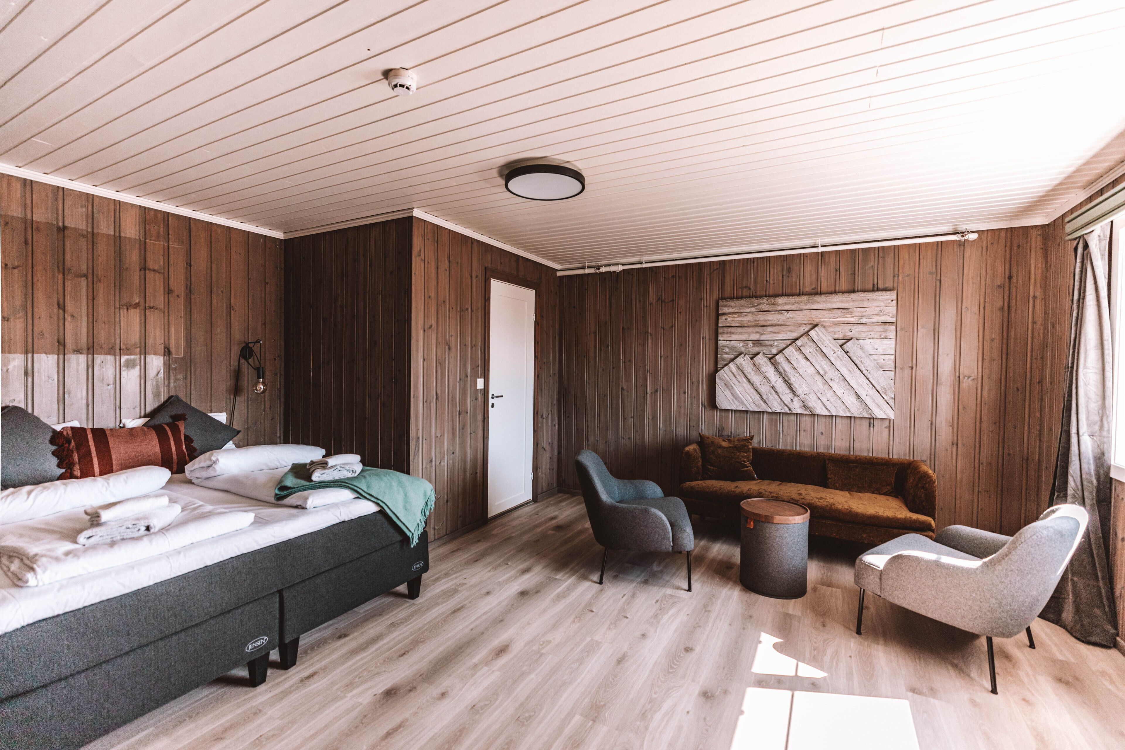 A room with a bed, a sofa, two armchairs, a small table, and a wall-mounted artwork.