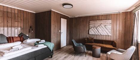 A room with a bed, a sofa, two armchairs, a small table, and a wall-mounted artwork.