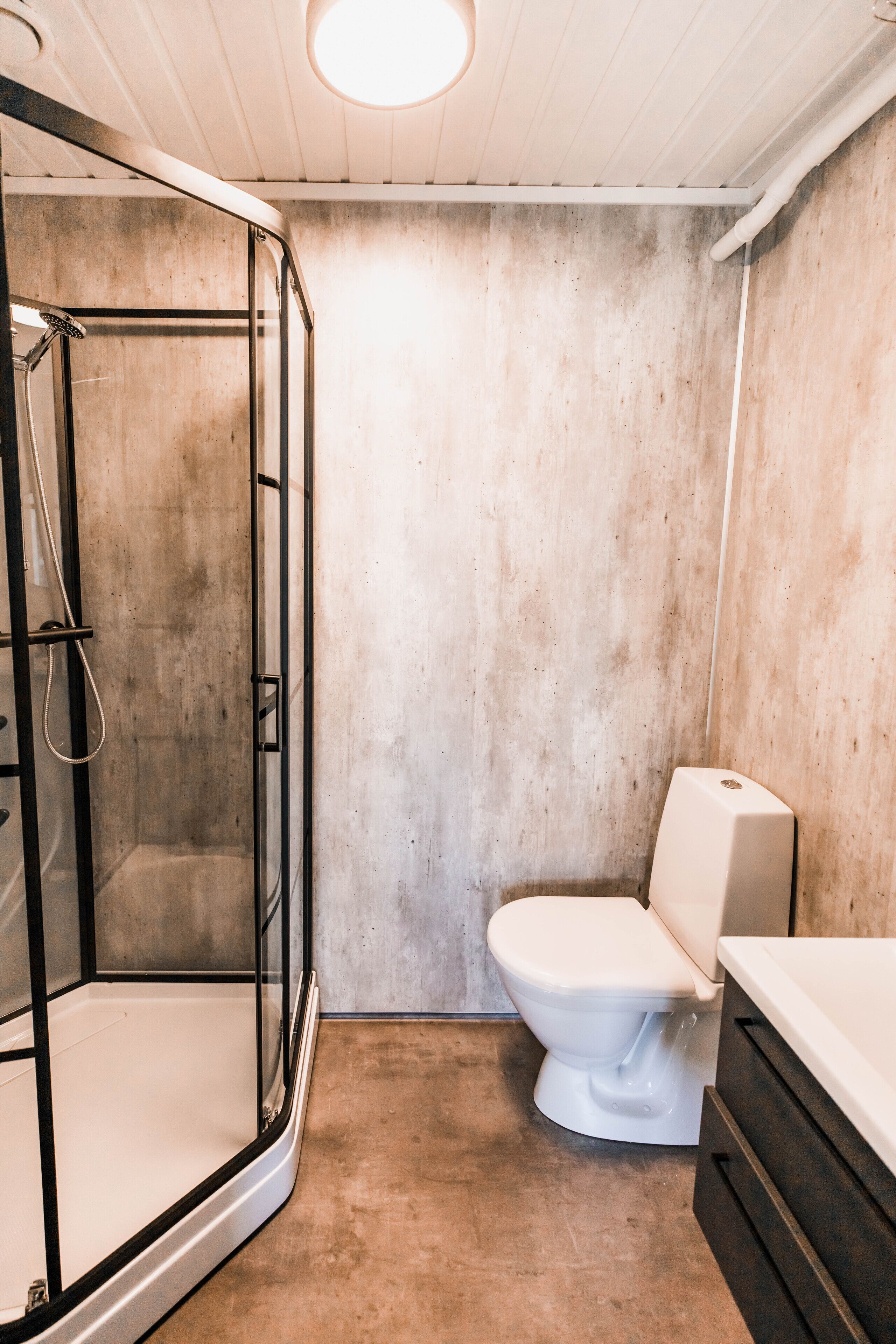 Ein Badezimmer mit einer gläsernen Duschkabine, einer Toilette und einem dunkel gefärbten Waschtisch.