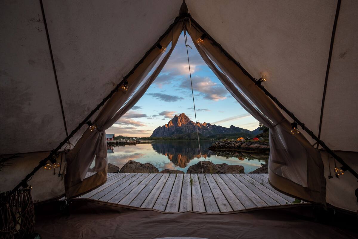 A tent with a wooden deck and a view of a mountain range reflected in a body of water.