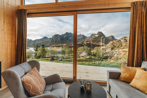 A modern room with a large window offering a view of mountains and a lake. There are two sofas and a small table with candles. - Skårungen (Vagan)