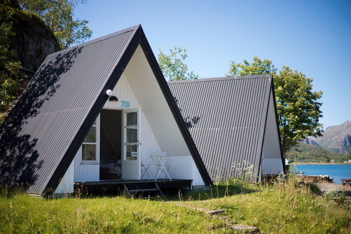 A modern, triangular-shaped cabin with a door marked "701" and a small outdoor seating area.