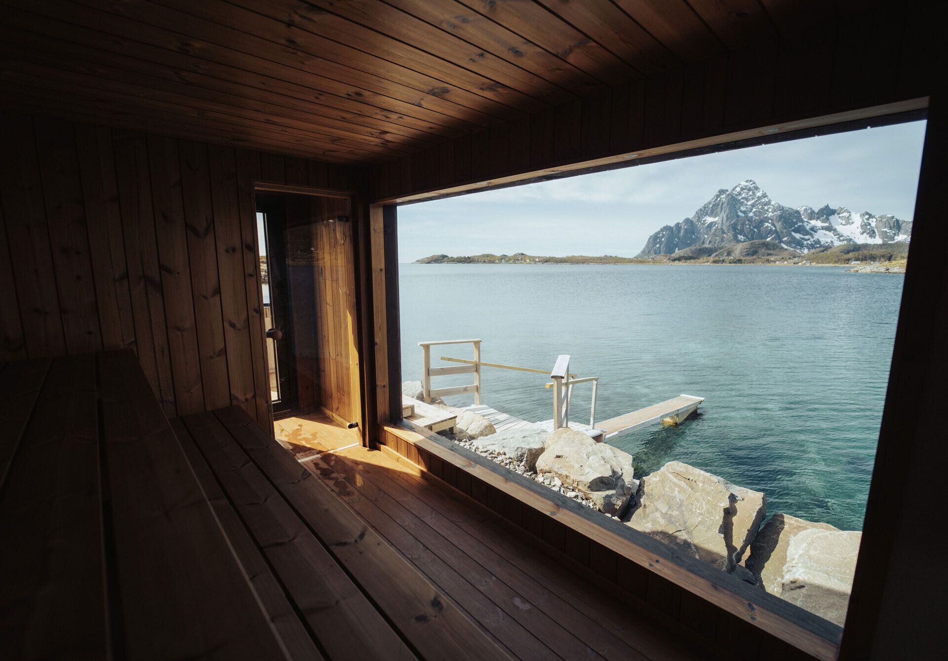 Una cabaña de madera con un ventanal grande que da a un lago tranquilo y una montaña.