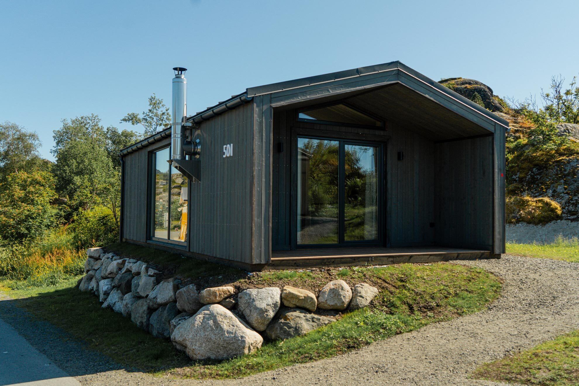 Una cabaña moderna con un amplio ventanal, una chimenea y cimientos de piedra.