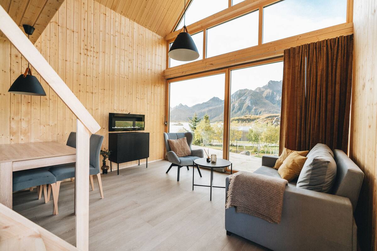A wooden interior with a dining area, a sofa, and a view of mountains.