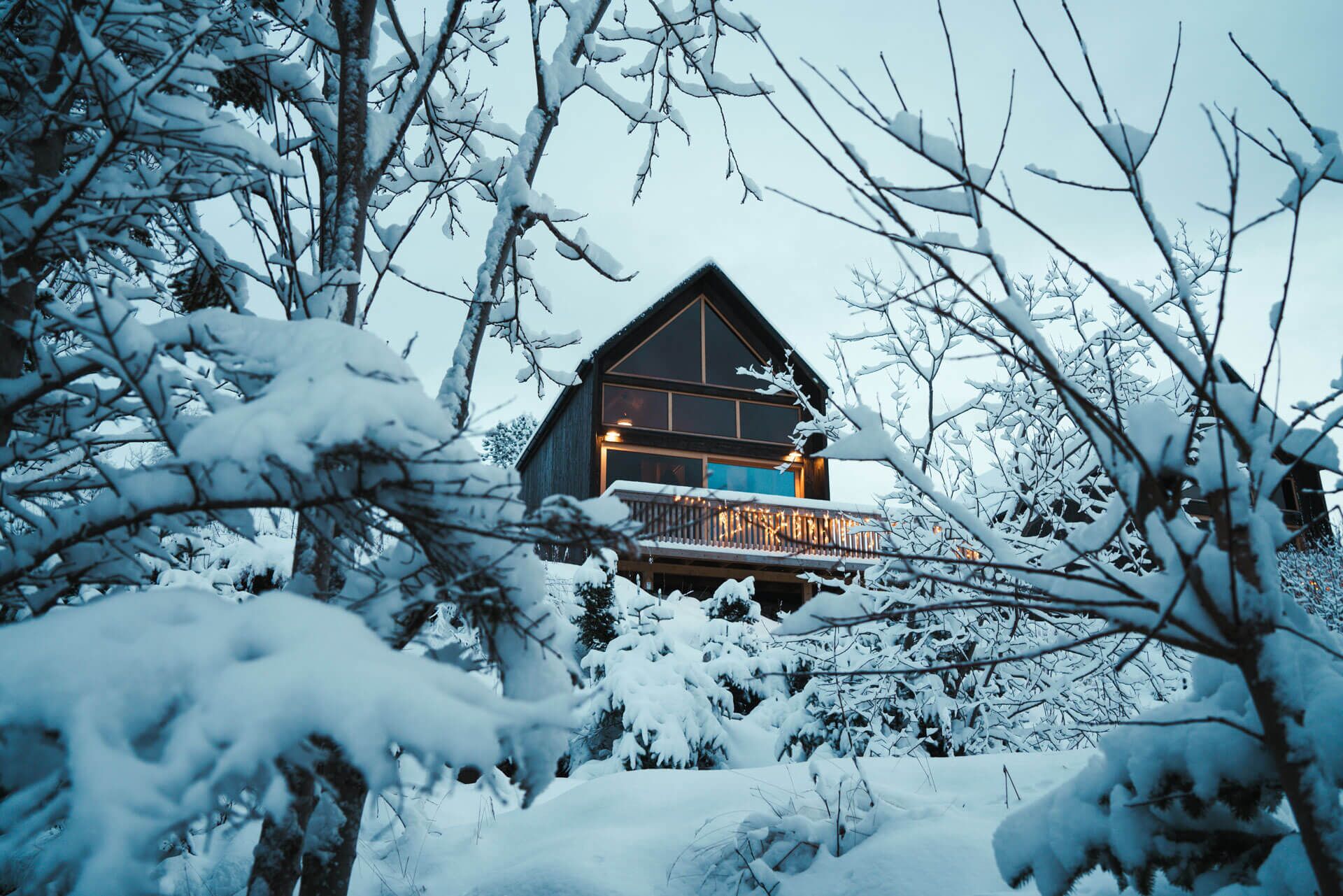 A cabin with a balcony, surrounded by snow-covered trees.