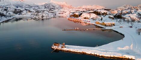 A snow-covered lakeside village with a dock extending into the water, surrounded by mountains.