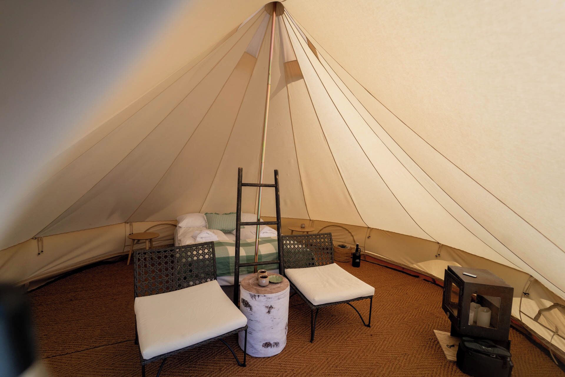 Een tent van binnen, met een bed, twee stoelen, een klein tafeltje en een televisie.