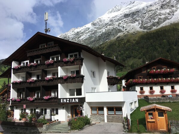 A traditional chalet-style hotel with balconies adorned with flowers, set against a backdrop of snow-capped mountains. - Gästehaus Enzian (Praegraten am Grossvenediger)