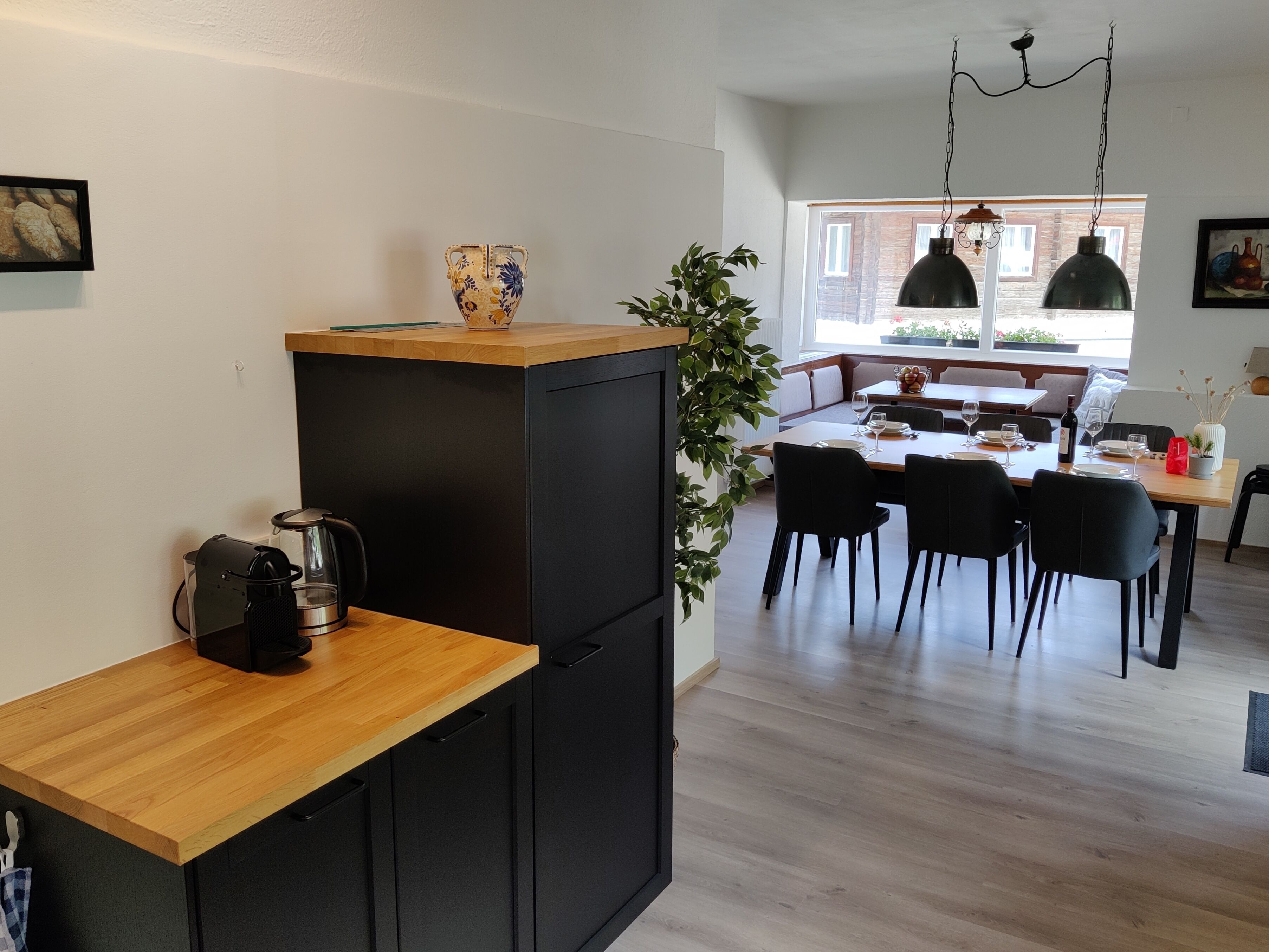 Une cuisine moderne avec un plan de travail en bois, des meubles de rangement noirs et un coin repas comprenant une table et des chaises en bois.