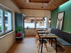 A cozy restaurant with wooden floors, a high ceiling, and a view of the outside. There are tables and benches for dining, and a large window with a view of the street. - Gästehaus Enzian (Praegraten am Grossvenediger)