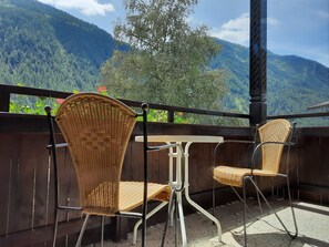 A balcony with wicker chairs and a table, overlooking a mountainous landscape. - Gästehaus Enzian (Praegraten am Grossvenediger)