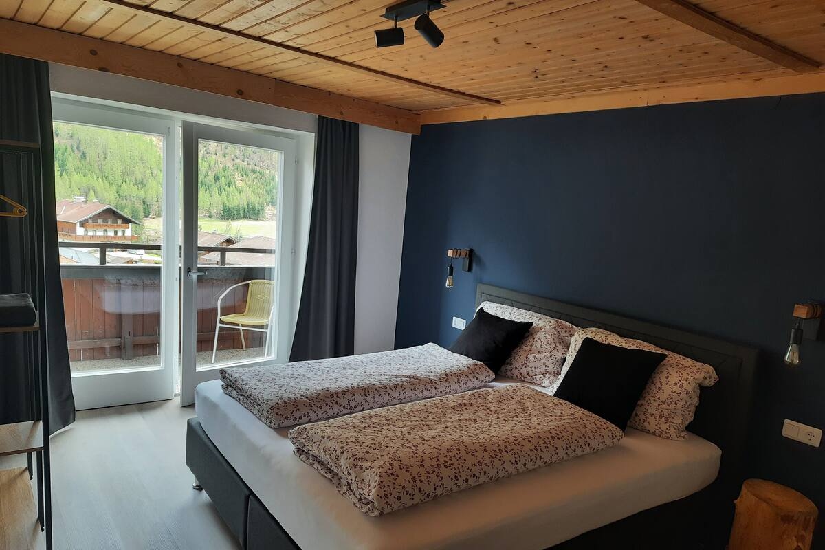 Ein Schlafzimmer mit einem großen Bett, Holzboden und Blick auf einen Balkon mit einem Stuhl.