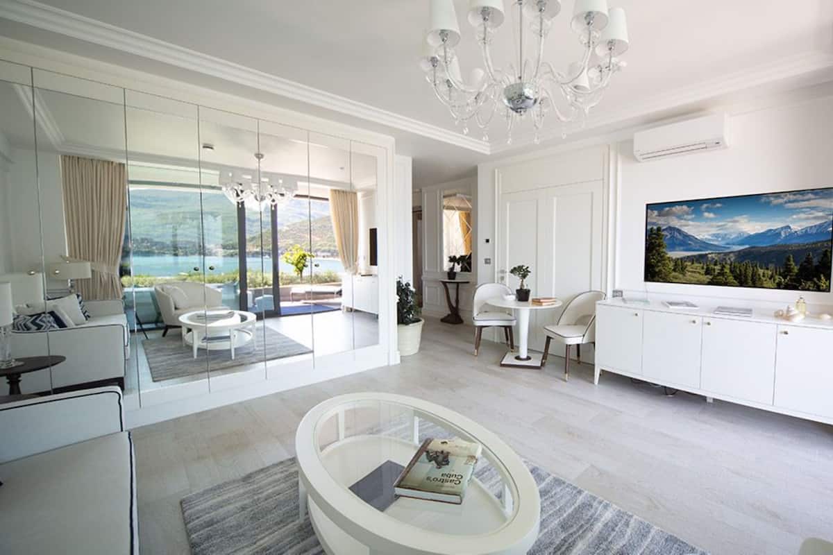 Un salon moderne avec un grand téléviseur, une table basse en verre et une vue sur les montagnes par la fenêtre.