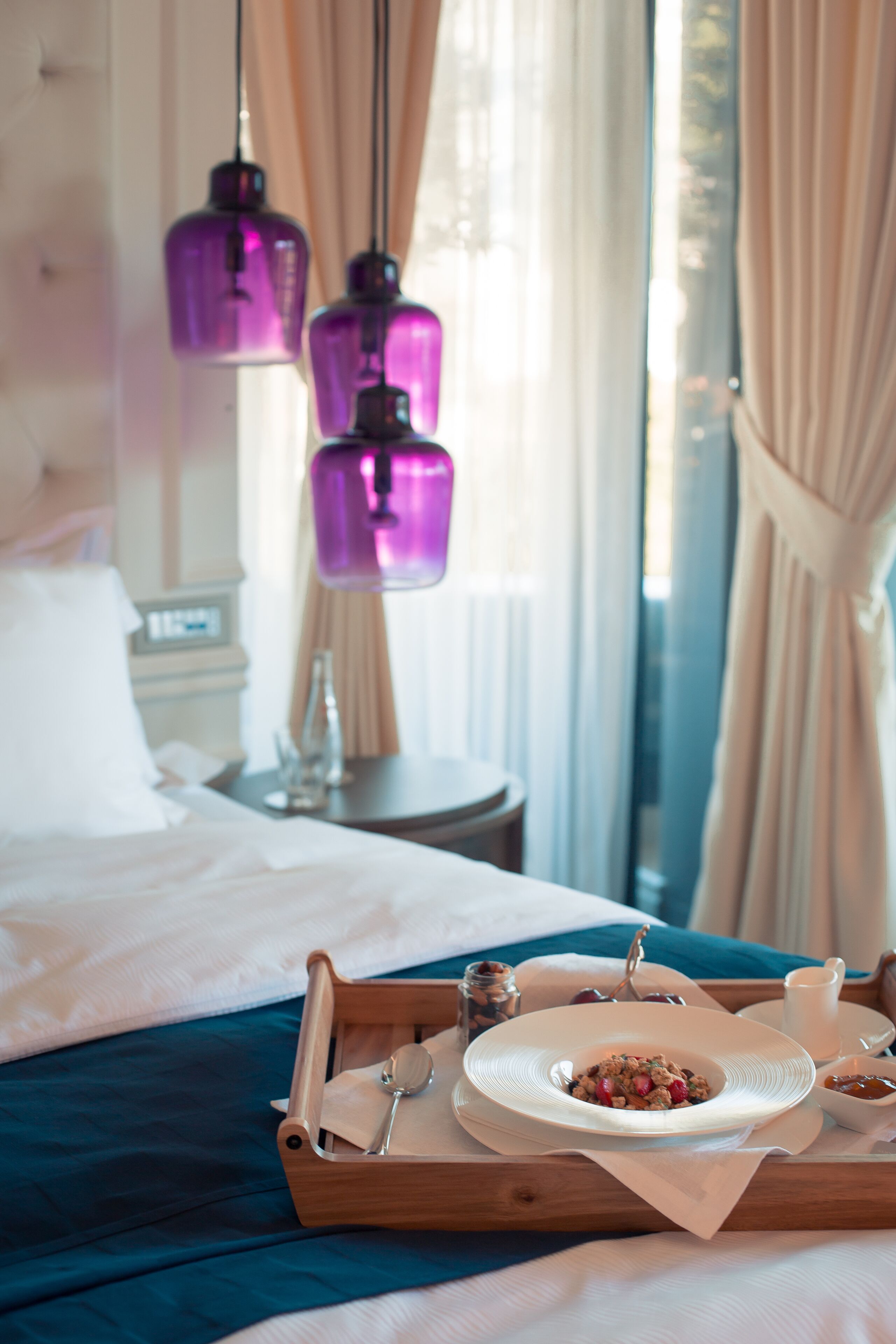 Una cama bien hecha con una bandeja de desayuno, que incluye cereales y fruta, en una habitación de hotel con vistas a la ciudad.