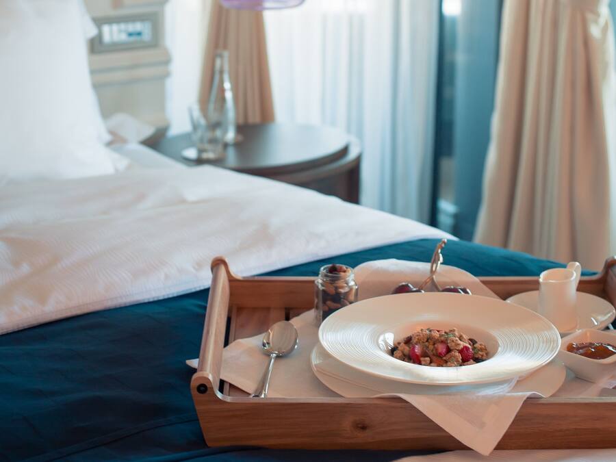 Una cama bien hecha con una bandeja de desayuno, que incluye cereales y fruta, en una habitación de hotel con vistas a la ciudad.