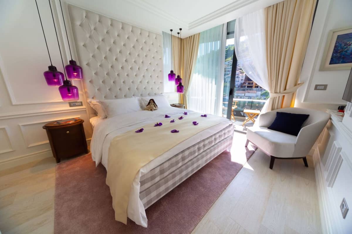 Une chambre d’hôtel avec un grand lit, une table de chevet, une chaise et une vue sur la ville grâce à de grandes fenêtres.