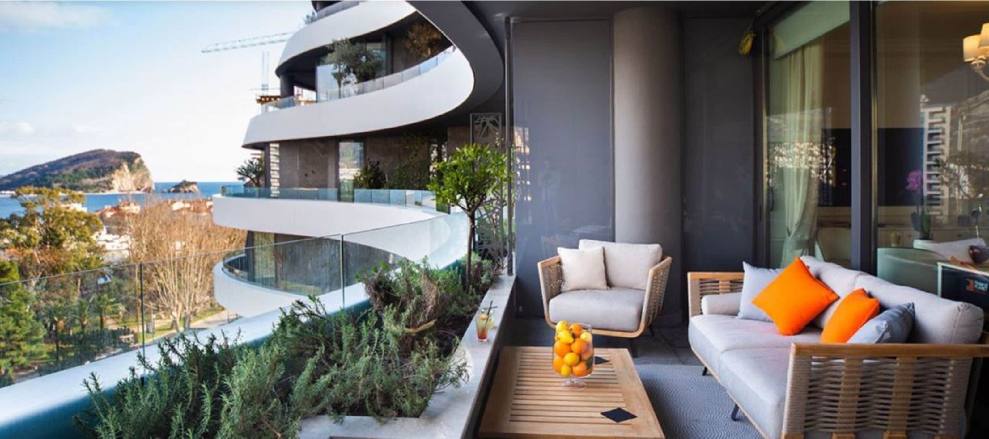Un balcón moderno con diseño curvo, mobiliario de mimbre y barandilla de vidrio con vista al litoral.