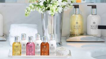 Un tocador de baño con una bandeja que contiene varios artículos de tocador Molton Brown, un jarrón con flores blancas y una toalla blanca.