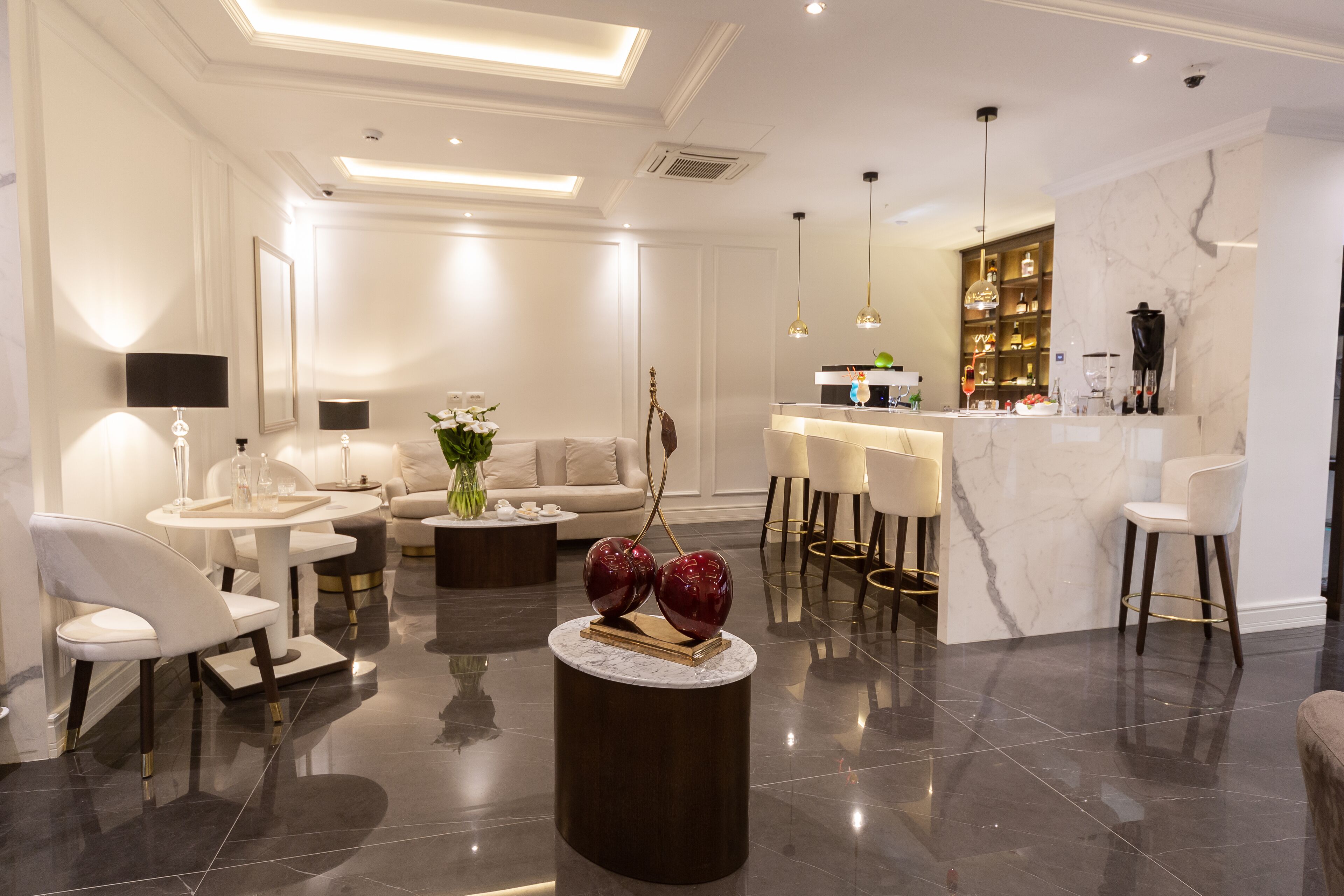A modern living room with a sofa, coffee table, and chairs. There is a dining area with a table and chairs. A kitchen area with a marble countertop and bar stools is visible.