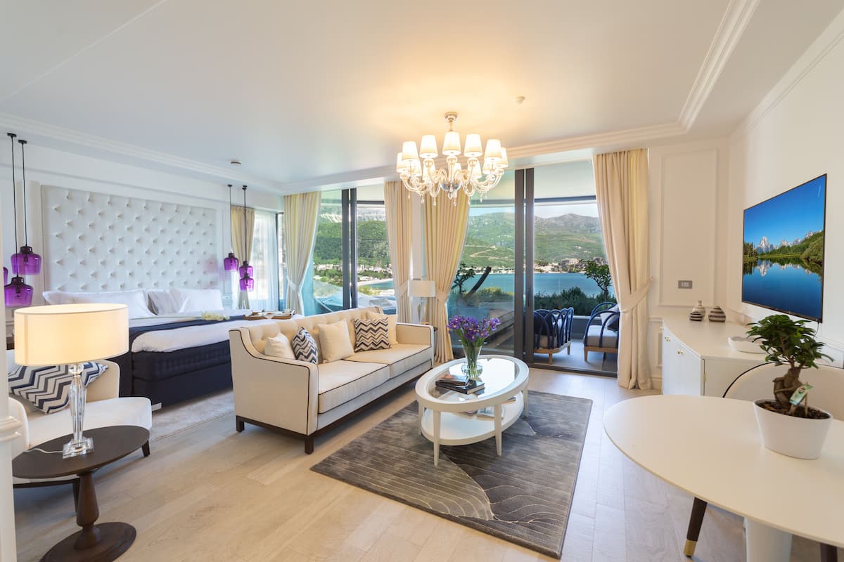 Un salon spacieux comprenant un grand lit, un canapé, une table basse et un téléviseur. La pièce est dotée de grandes fenêtres offrant une vue sur un lac et des montagnes.