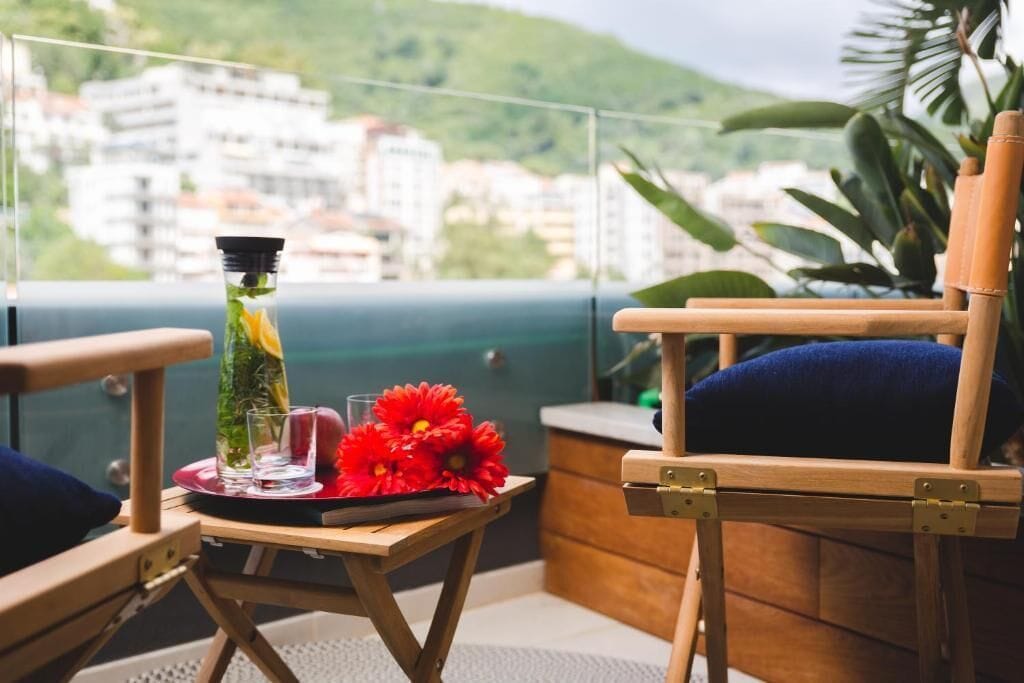 A balcony with a table set for two, a bottle of water, and red flowers.
