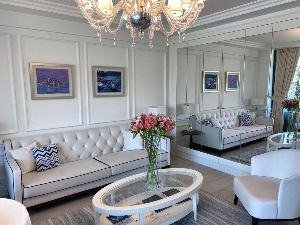 A modern living room with a white sofa, a glass coffee table, and a chandelier.